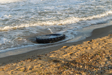 旧黑色橡胶轮胎遗留在海滩环境污染概念选择性焦点彩色色调图片。 在海滩上蓝色的水中丢弃的旧轮胎。 海洋和海滩上的污染和垃圾