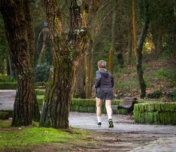 一名高级男子在绿色森林公园跑步的后视镜。 灰发跑步服装和短裤。