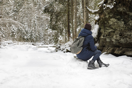 带背包的女孩坐在白雪覆盖的针叶林里。 冬季阴天
