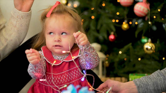 小女孩和大人玩花环。一个小女孩拿着一棵圣诞树的背景上的花环