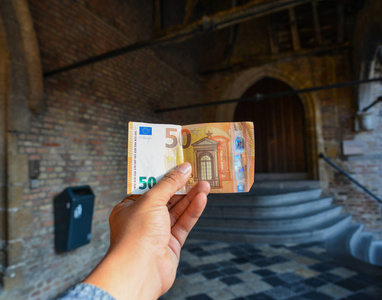 男性手拿着一张折叠的50欧元，上面有旧建筑背景。