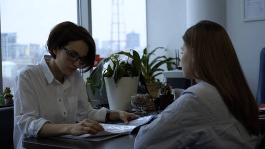 两名女商人在任期间签下了合同。年轻的有魅力的女商人在看文件后达成一致, 并握手。成功交易