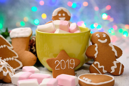 姜饼干和棉花糖在杯上白色背景与圣诞树, 蜡烛和圣诞灯
