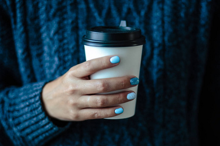 华丽的指甲粉，嫩蓝色指甲油特写照片。 女性手拿着塑料咖啡杯，背景简单