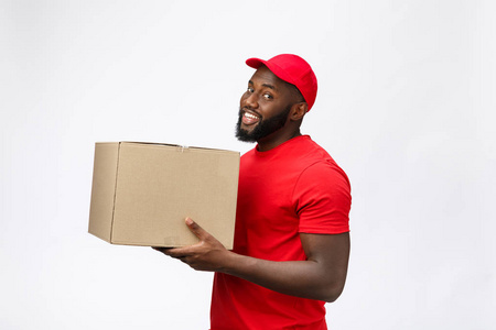 交付概念侧视图的角度快乐非洲裔美国人交付男子在红布拿着一个盒子包。在灰色背景上隔离。复制空间