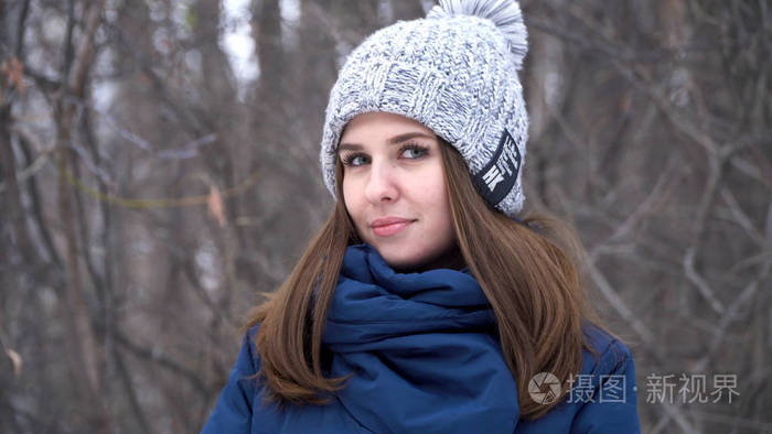 照片 穿着冬帽的漂亮女人微笑着站在外面的雪地上, 在森林里, 有雪楼