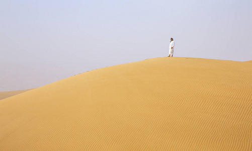 穿着传统阿联酋服装在里瓦沙漠大沙丘上行走的男人