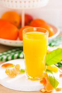 橘子汁在玻璃和新鲜水果与叶子白色木制厨房背景特写。 健康可口的清爽夏日饮料