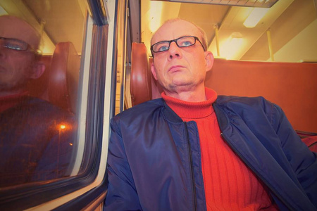 中年男人从火车的窗户往外看。 乘欧洲高速快车旅行时的乘客。 老人晚上乘火车旅行。