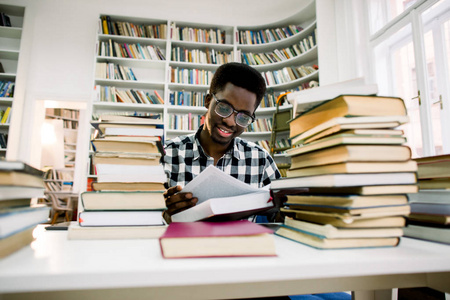 性格开朗皮肤黝黑的男学生花时间在图书馆的Autodidact上，书积极，非裔美国人时髦的家伙，对有趣的畅销书阅读当代文学感