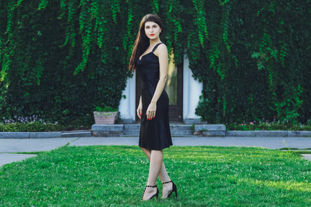 一个年轻漂亮的黑发女孩，穿着黑色的裙子，在绿草的背景下的夏天公园里