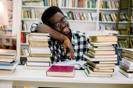非裔美国男大学生坐在图书馆的桌子上看书。 眼镜上文件的反射。 水平形状正面视图
