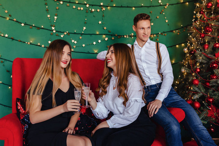 一家年轻的公司，两个女孩和一个男人在家里拿着一杯香槟庆祝新年