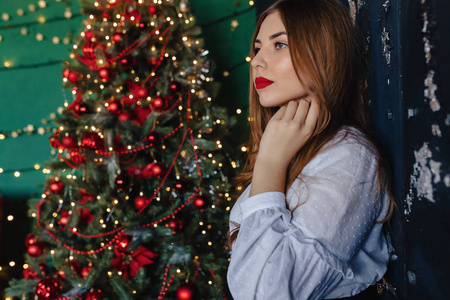 年轻漂亮的女孩穿着节日服装，背景是圣诞树，主题是新年