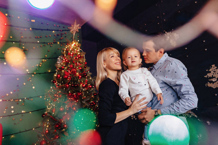 可爱的年轻家庭带着小宝宝在圣诞树的背景上庆祝新年