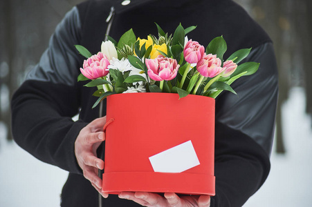 男人拿着红色的礼盒，带着美丽的鲜花，浪漫的时刻，女人的日子和情人节。 送快递的人送花盒。 复制空间