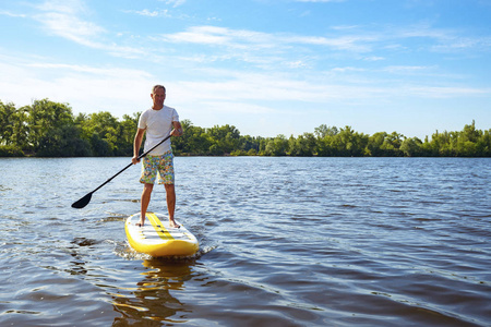 快乐的人在晴天在一条大河上的SUP板上划水。站起来划桨登机在大自然中令人敬畏的积极娱乐。