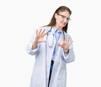 中年成熟的医生女人穿着医用外套，在孤立的背景下，厌恶的表情不悦和恐惧的做厌恶的脸，因为厌恶的反应。 举起双手。 令人讨厌的概念
