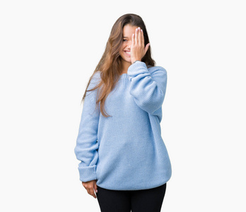 年轻漂亮的黑发女人，穿着蓝色的冬季毛衣，在孤立的背景上，用手遮住一只眼睛，脸上带着自信的微笑惊讶的情绪。