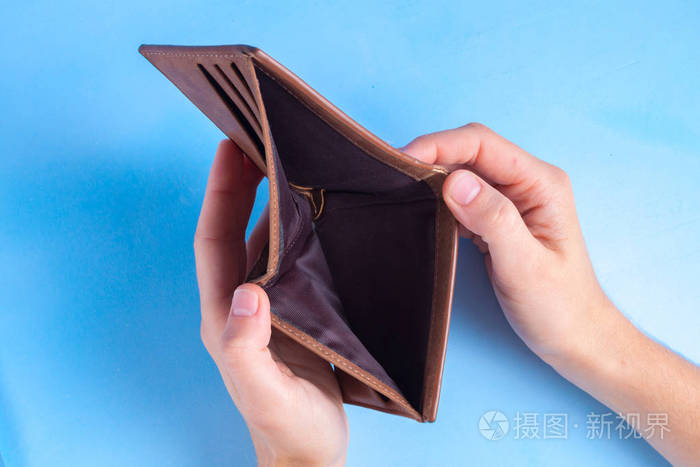 一个男人拿着一个蓝色背景上的空钱包金融危机钱的问题缺钱