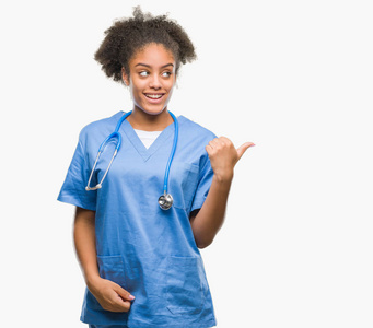 年轻的非洲美国医生女人在孤立的背景上微笑，快乐的脸看着，并指向一边，拇指向上。