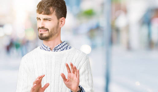 年轻的帅哥穿着冬天的毛衣在孤立的背景下厌恶的表情，不高兴和恐惧做厌恶的脸，因为厌恶的反应。举起双手。令人讨厌的概念。