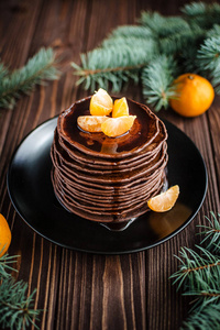 一堆自制的巧克力薄煎饼，上面有巧克力布丁和木制背景的橘子