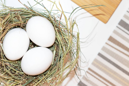 新鲜的白鸡蛋在白色桌子上的草窝里覆盖着条纹布。