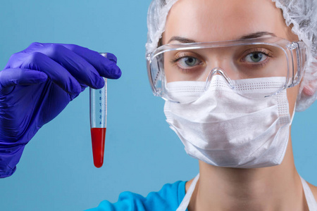 戴眼镜的实验室助理戴医用口罩医用手套实验室制服装有血液的试管。 实验室医学测试和研究。