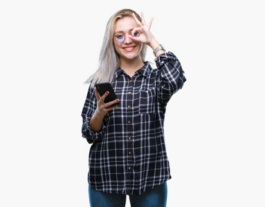 年轻的金发女人用智能手机发短信，在孤立的背景下发送信息，快乐的脸，微笑，做好的签名，用手盯着手指看。
