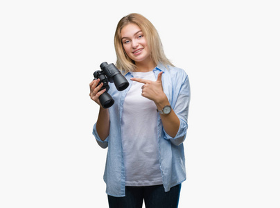 年轻的白种人女人拿着双筒望远镜在孤立的背景上非常高兴地用手和手指指点