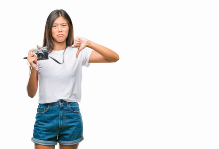 年轻的亚洲女人拿着vintager a照相机在孤立的背景上，愤怒的脸，负面的标志，显示不喜欢，拇指向下拒绝的概念