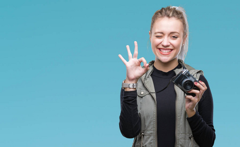年轻的金发女人用老式相机在隔离的背景上拍照，做OK标志，手指，优秀的符号