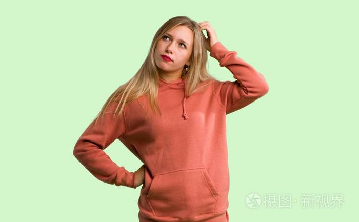 在绿色背景下挠头时产生疑问的年轻女孩