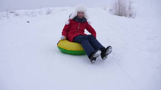 快乐的孩子在雪橇上的雪滑梯上滑行, 管道。女孩在公园里玩冬天的游戏。欢快的少女在白色的帽子和红色夹克有一个笑