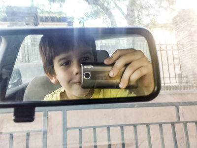 孩子用电话拍照。 车镜和带电话的男孩。