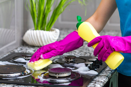 家庭主妇戴着彩色橡胶手套，在厨房里用洗涤剂洗煤气炉。 房屋清洁