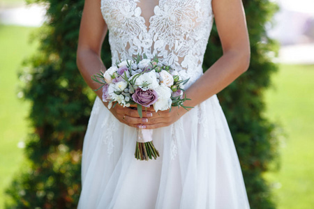 新娘站在绿色的背景上，拿着一束紫色的花，白色的花和绿色的植物，带着柔和的丝带。