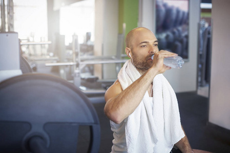 运动的男人在锻炼后坐在健身房喝了一瓶水。