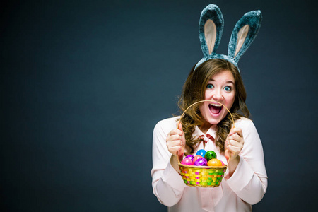 摄影棚拍摄一个快乐的年轻女人戴着兔子耳朵，拿着一个五颜六色的复活节鸡蛋