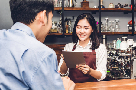 女小企业主在咖啡馆柜台后面工作的肖像。Barista使用平板电脑并收到客户的订单