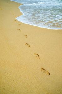 海滩旅行女人在沙滩上放松散步，在沙滩上留下脚印。金色沙滩上女性脚和腿的特写细节