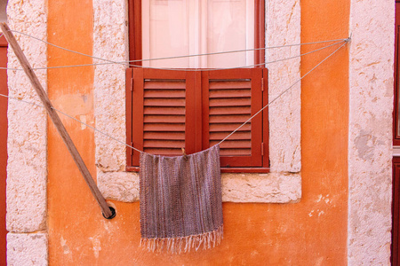 绳子上的毛巾靠在橙色风化的墙上。 紧闭的窗户，旧墙上有百叶窗和干燥的亚麻布。 葡萄牙的建筑立面。 旅行概念。 欧洲建筑。 葡萄牙