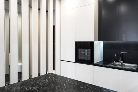 舒适屋的豪华内部侧面视图。 厨房家具的白色和黑色立面，新的烤箱和水龙头，水槽