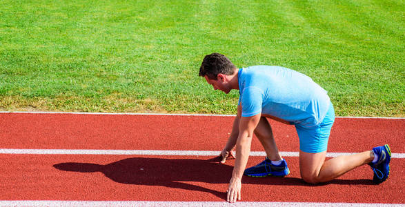 运动动机的概念。男运动员运动员站在低起跑位置体育场路径阳光明媚的日子。为胜利而努力。赛跑者准备好了。成人跑步者在体育场准备比赛。