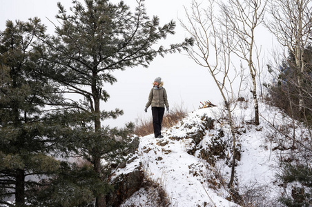 徒步旅行 一个女孩沿着松树和其他树木之间的小路爬上山上的雪顶