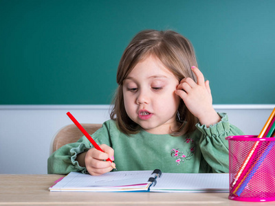 小漂亮女孩坐在教室里的灰色桌子上画画。