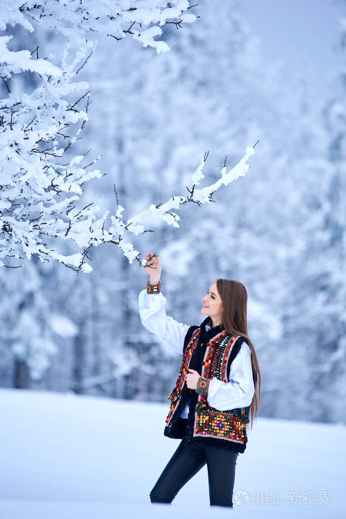 穿着白色刺绣上衣和五颜六色的背心,在冬天的白天在雪景背景下户外