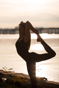 年轻女子在河滩和城市背景下练习瑜伽。