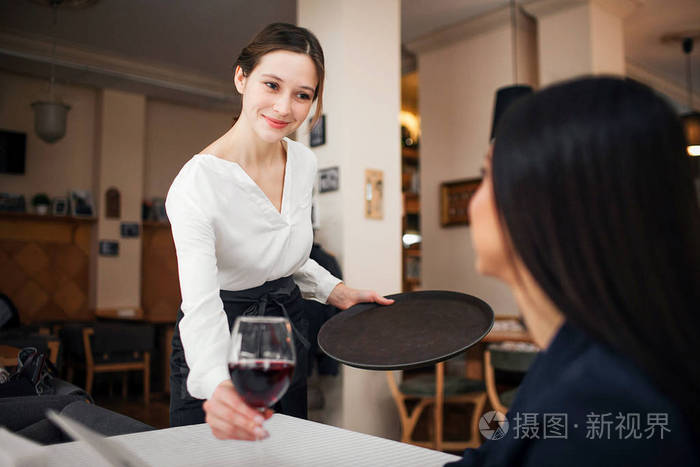 开朗礼貌的年轻女服务员看着顾客微笑 她把一杯酒放在桌子上.